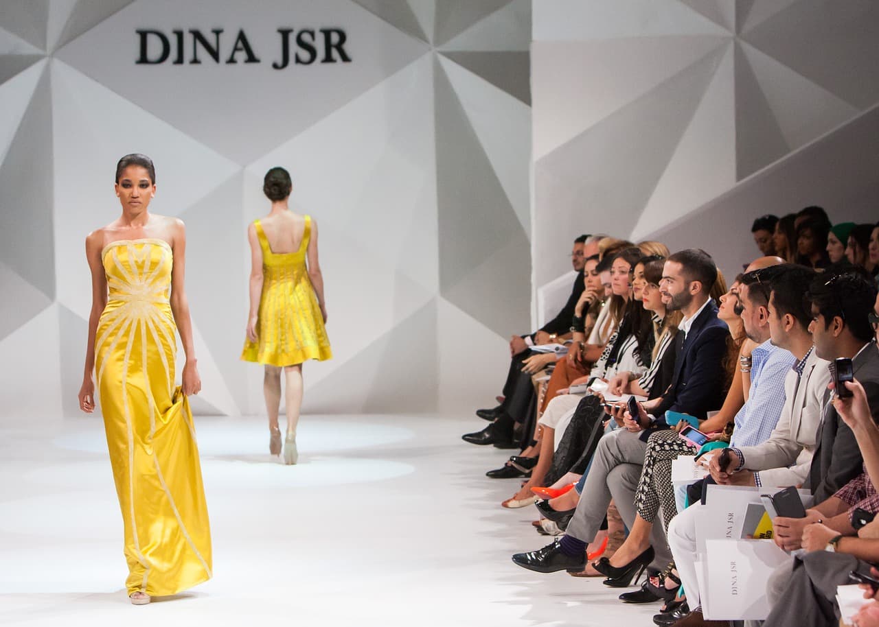 Models in yellow dresses on a catwalk in front of a seated front row