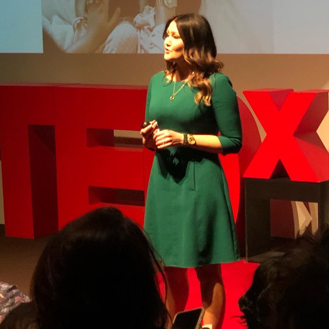 A speaker in a green dress presenting on a TEDx stage