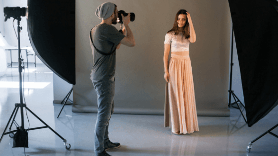 A photographer shooting a model in a long blush gown on a studio set