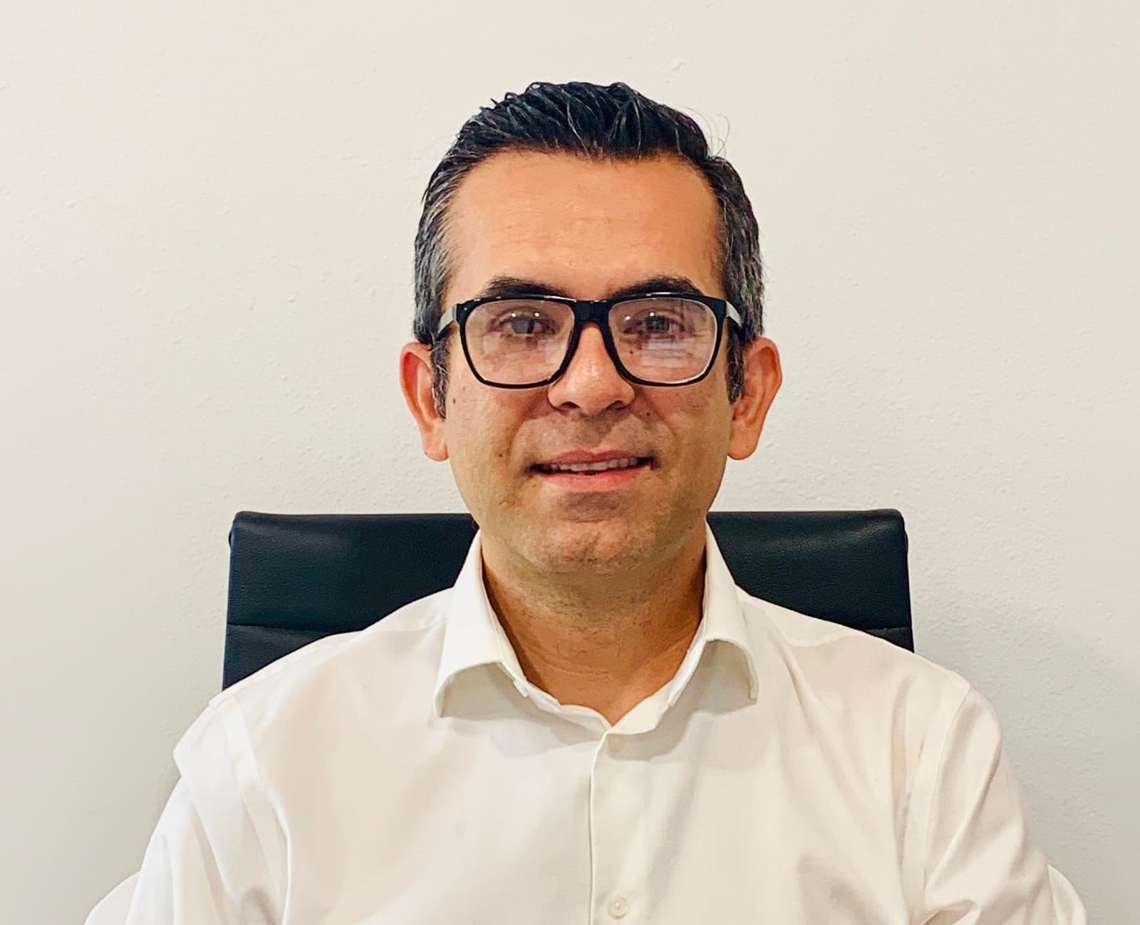 Portrait of a man in glasses and a white shirt seated in an office chair