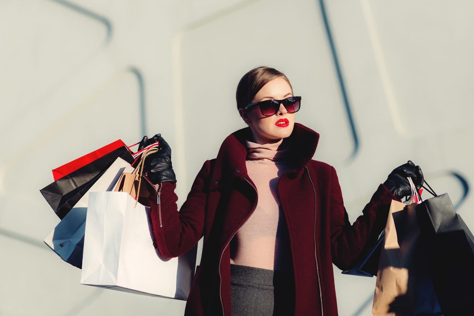 A woman in a burgundy coat and sunglasses carrying several shopping bags