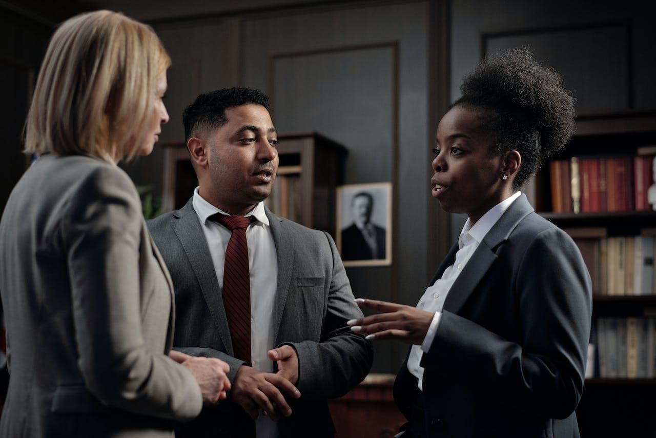 Three people in business suits talking in a wood panelled office