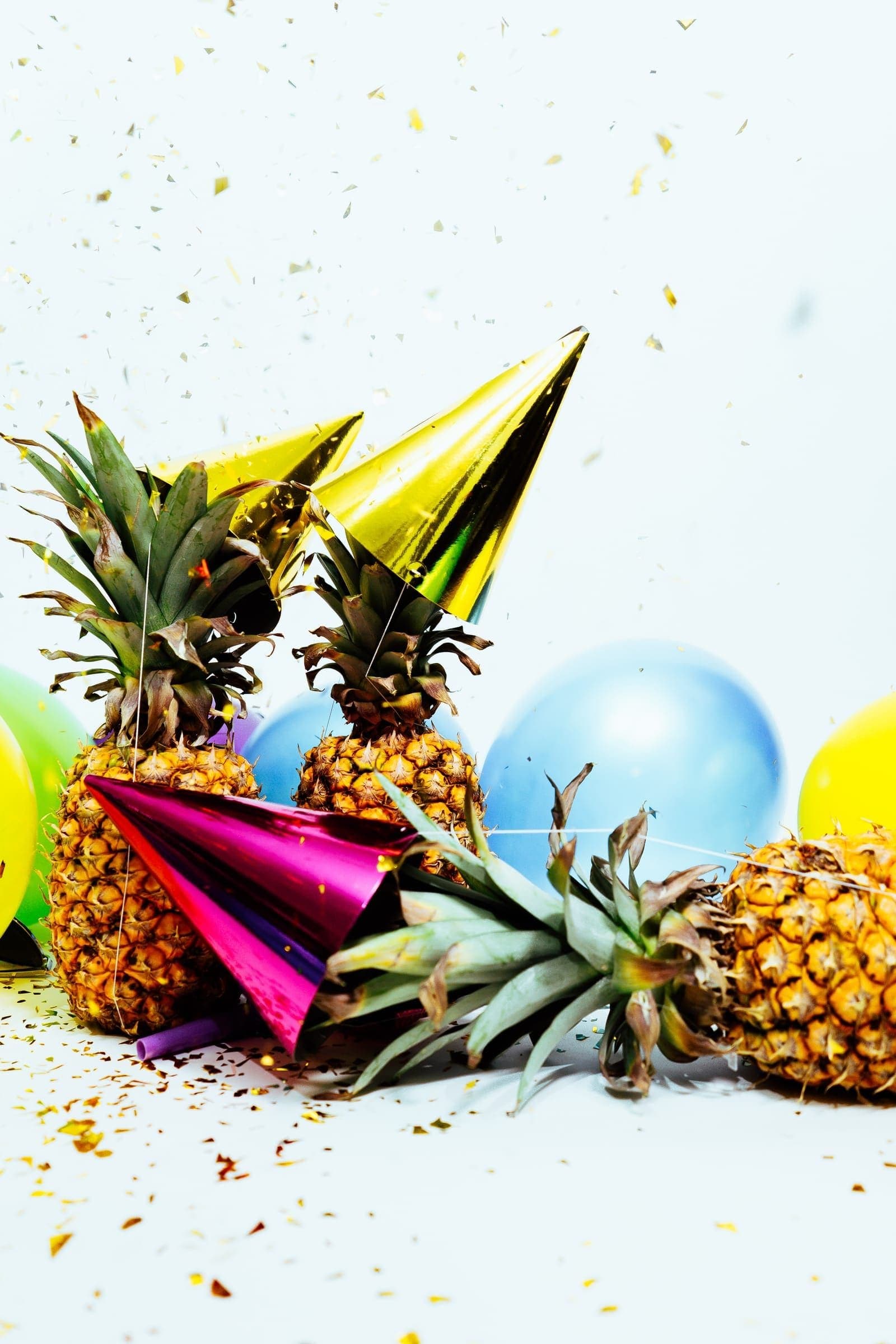 Pineapples wearing party hats among balloons and gold confetti